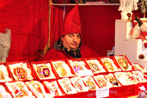 A funny male vendor wearing tall red gnome hat is sitting inside the Christmas market stall on Højbro Plads square