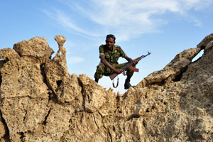 Afar security guard with an assault rifle is under the spindrift clouds