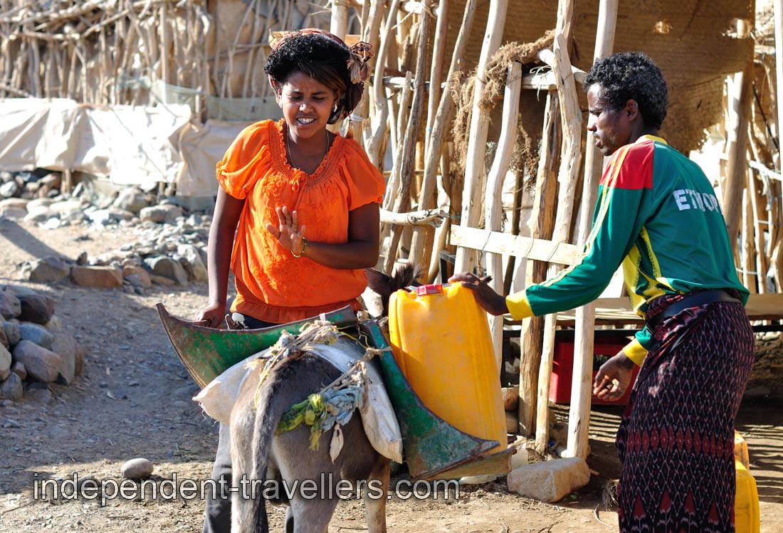 Lady takes part in the process of loading of the water containers on the donkey