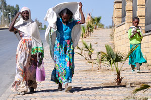 Two Ethiopian women and one girl walk along the wall of Martyrs' Memorial Monument