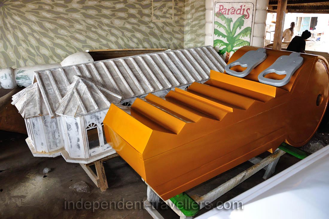 A coffin in the shape of an orange key is in the Kane Kwei Carpentry Workshop