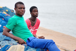 Two Ghanaian men are sitting on the pile of fishing nets