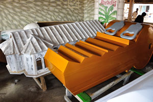 A coffin in the shape of an orange key is in the Kane Kwei Carpentry Workshop