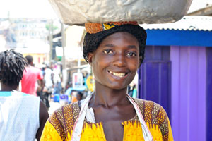 A lovely Ghanaian young woman smiles at me while carrying the basin full of plastic jerry cans