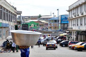 A woman with a bowl on the head walks down the Nyarko Kusi Amoah street