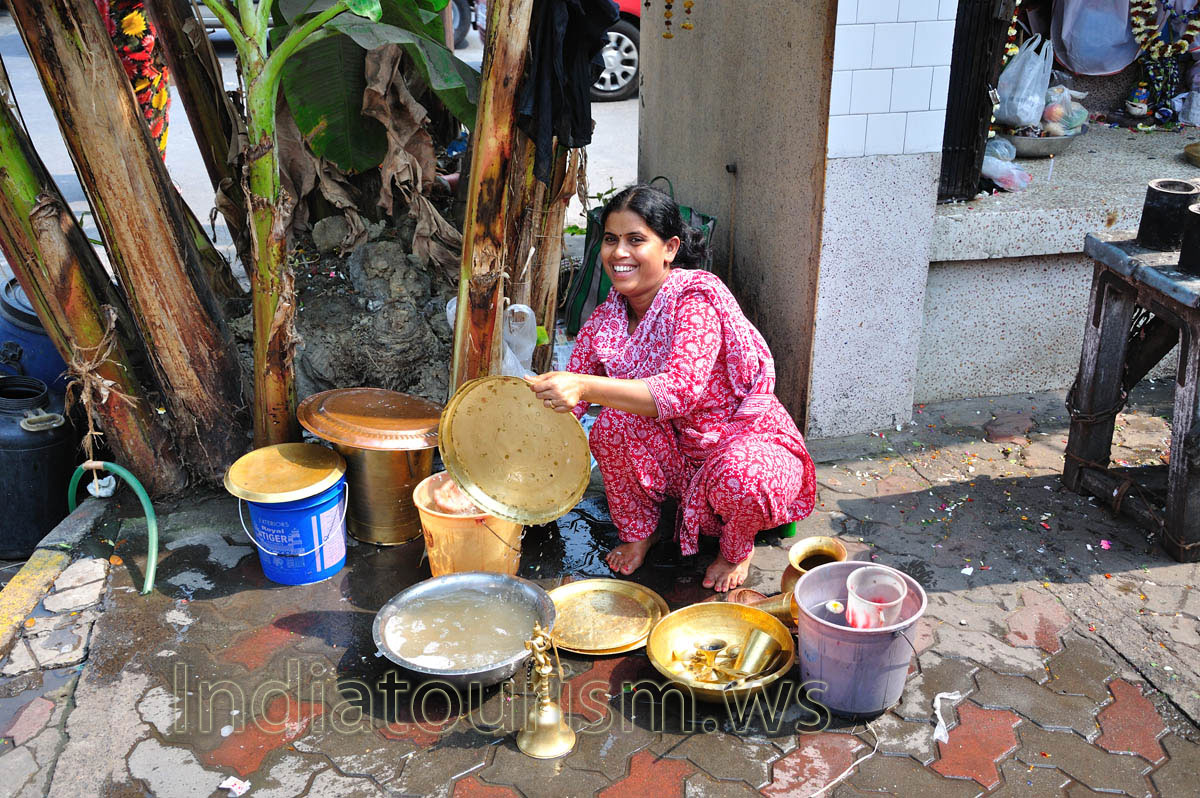 Woman on the street washes brass utensils