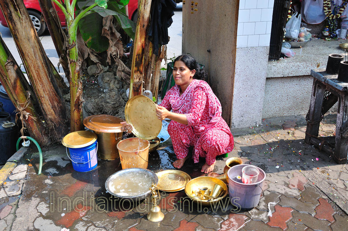A woman in a smart dress washes dishes under banana trees