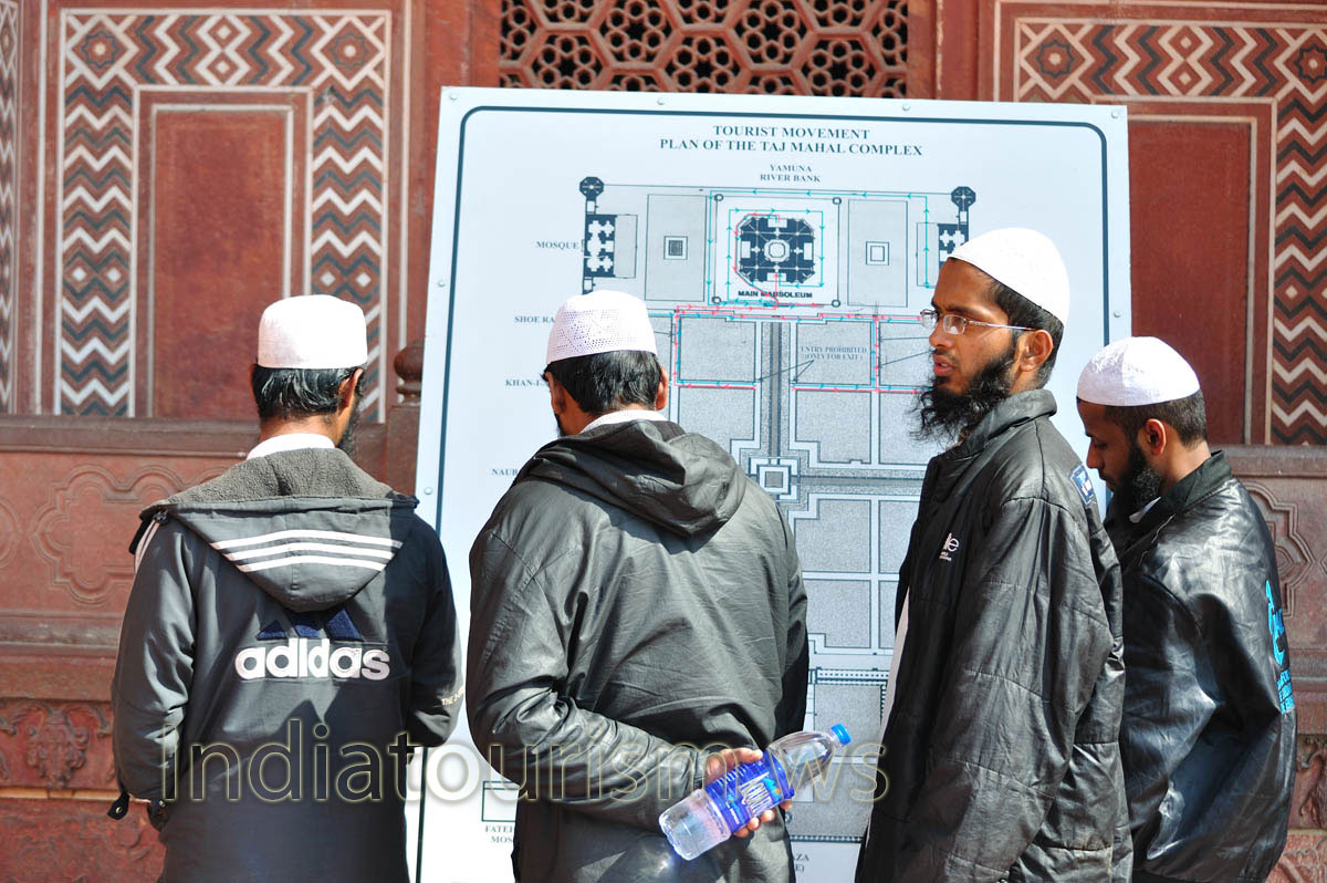 four muslims in black jackets and white caps are studying plan of the Taj Mahal
