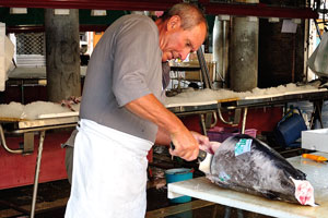 A hard-working vendor cuts a slice from a swordfish