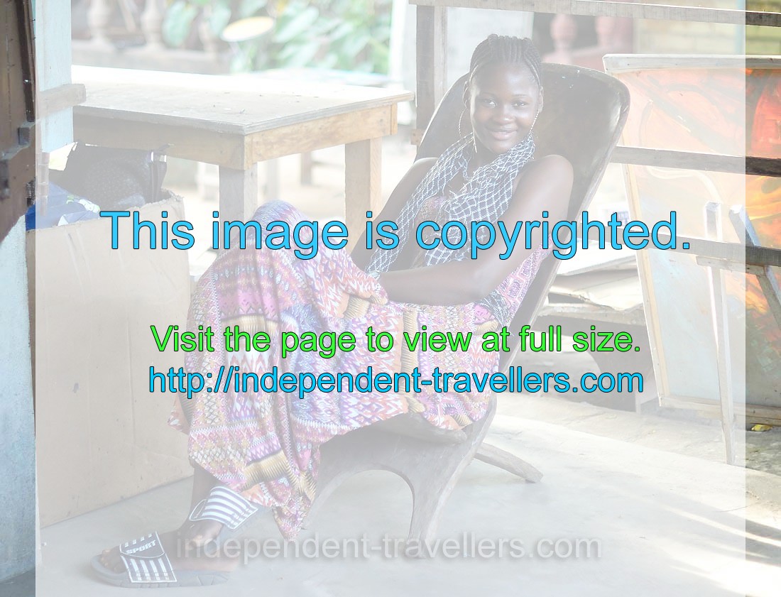 An attractive Ivorian girl is sitting in the wooden armchair on the CAVA souvenir market