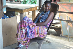 An attractive Ivorian girl is sitting in the wooden armchair on the CAVA souvenir market