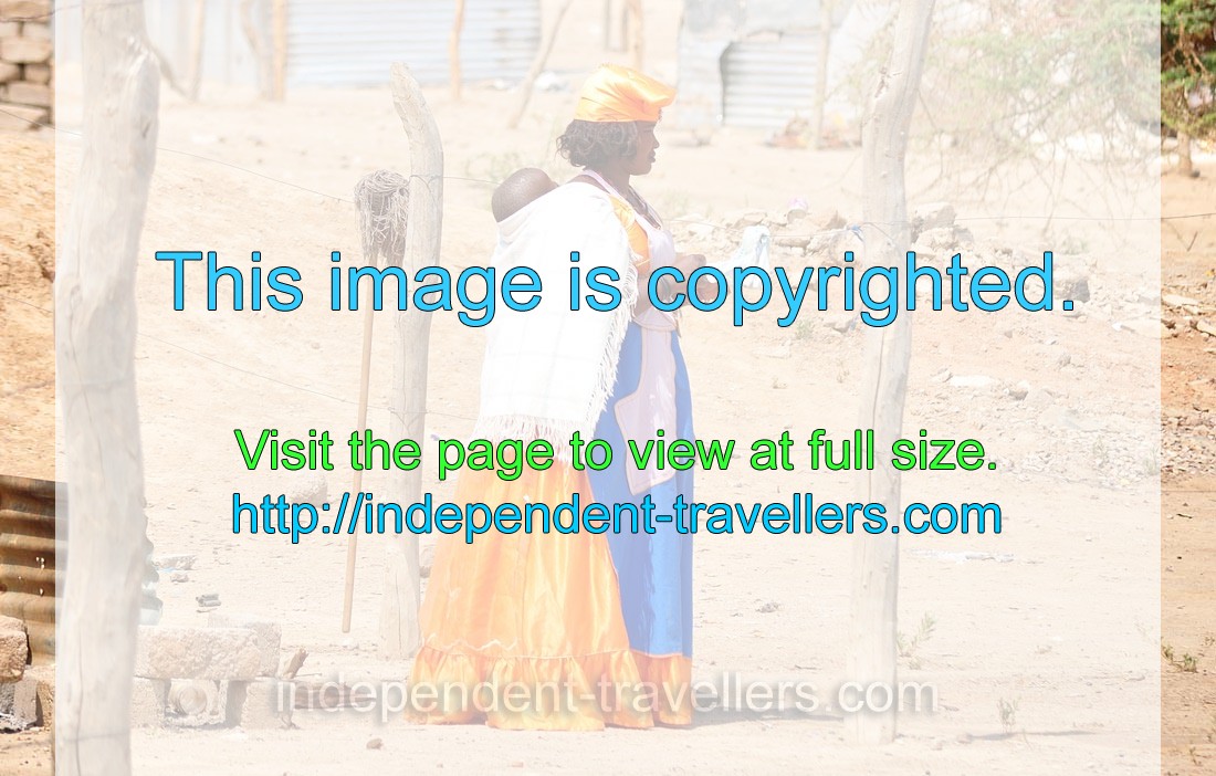 A Herero woman with a baby wears a blue-orange dress