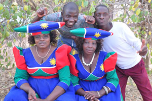 Two boys want to be photographed with Herero women dressed in the national clothing with the colours of the Namibian flag