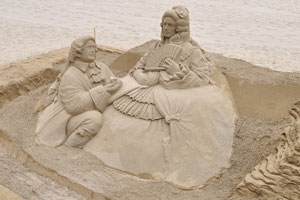 Sand sculptures and the blue lounge chairs are on the beach of Las Canteras