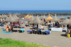 Numerous sun loungers and parasols with straw roofs are placed on Playa de El Bobo beach