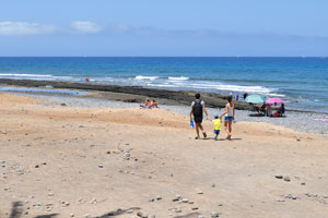 A young couple is walking with the child along Playa de las Américas beach