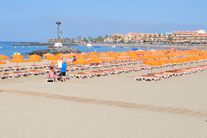 Numerous orange parasols are on Playa de Las Vistas beach