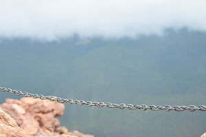 The metallic chain is in focus on the background of clouds floating below Mount Teide which are out of focus