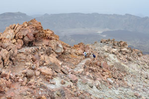 A couple of tourists are on the stone footpath lying along the Mount Teide crater