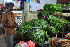 A male vendor sells piles of leafy vegetables