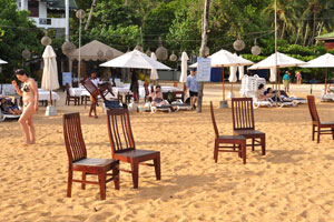 Wooden chairs are on the sand before a sunset