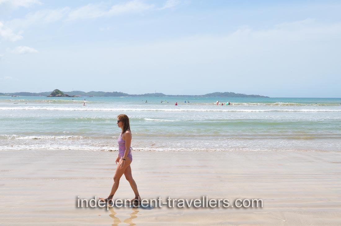 A woman walks along the shore of Weligama Beach