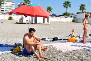 A young Turkish man is sitting on the shingle beach
