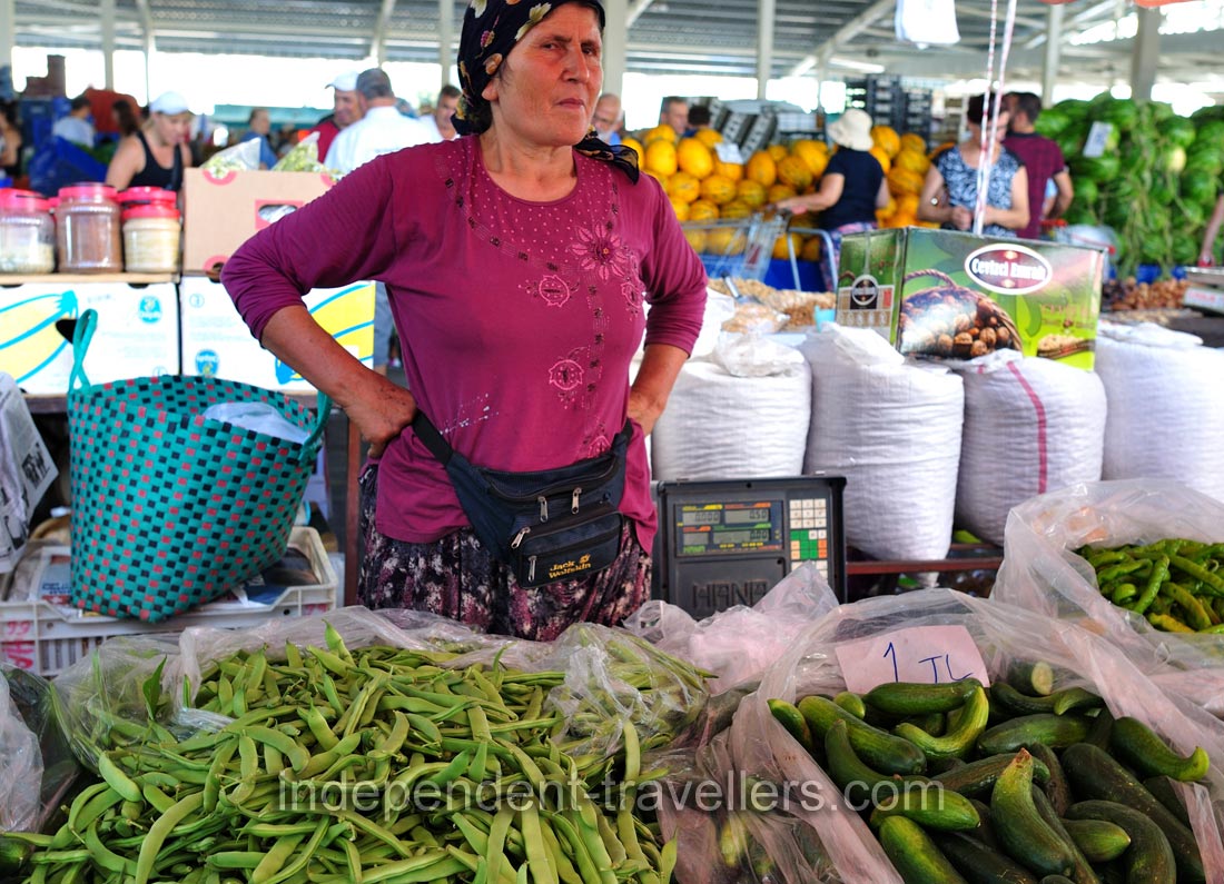 A female vendor sells green beans and cucumbers for 1 turkish lira per 1 kg