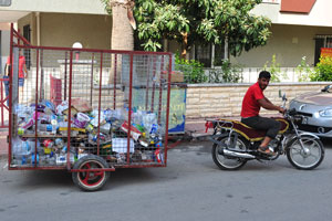 A man uses a motorbike with a special trailer to transport garbage along the city