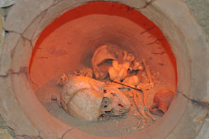 A skull and bones lie with a pitcher inside a burial chamber