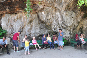 Tourists rest on benches under a cliff